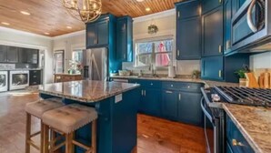 Una cocina moderna con armarios azul oscuro, una isla central y techo de madera.