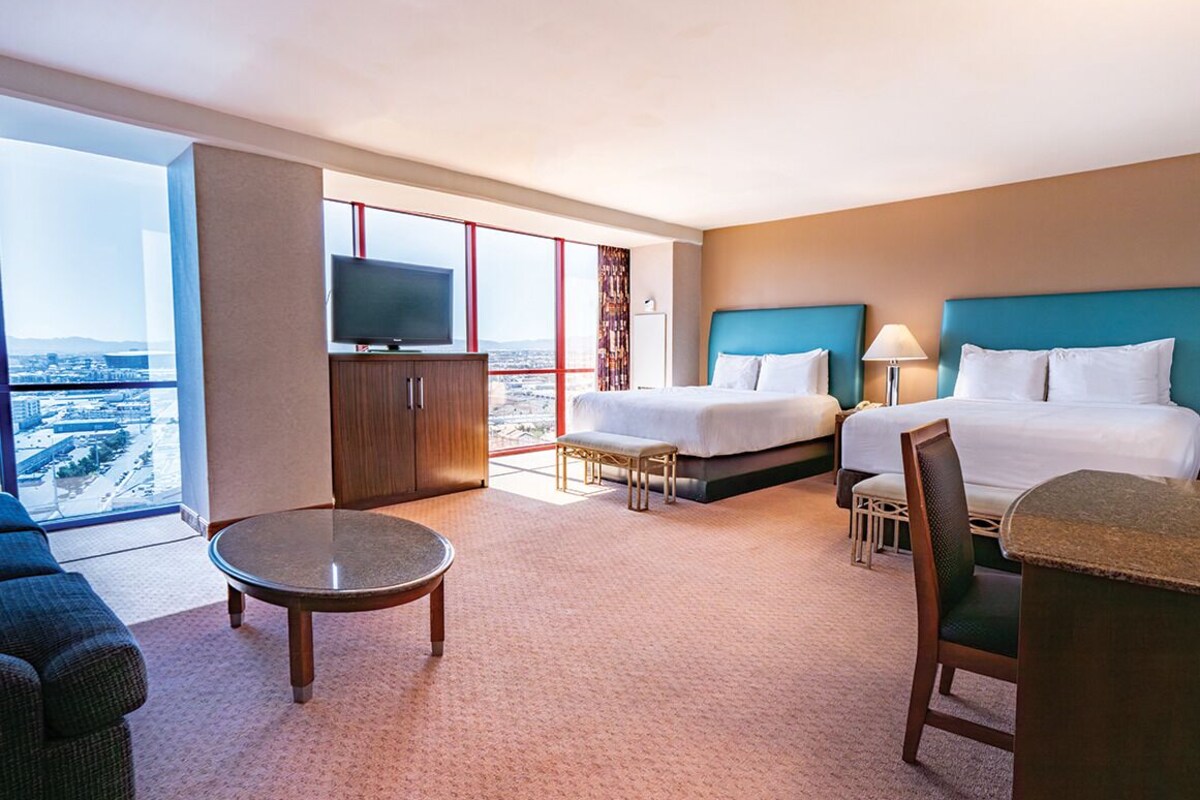 Quarto de hotel com duas camas, televisão, uma mesa pequena e vista para a cidade.
