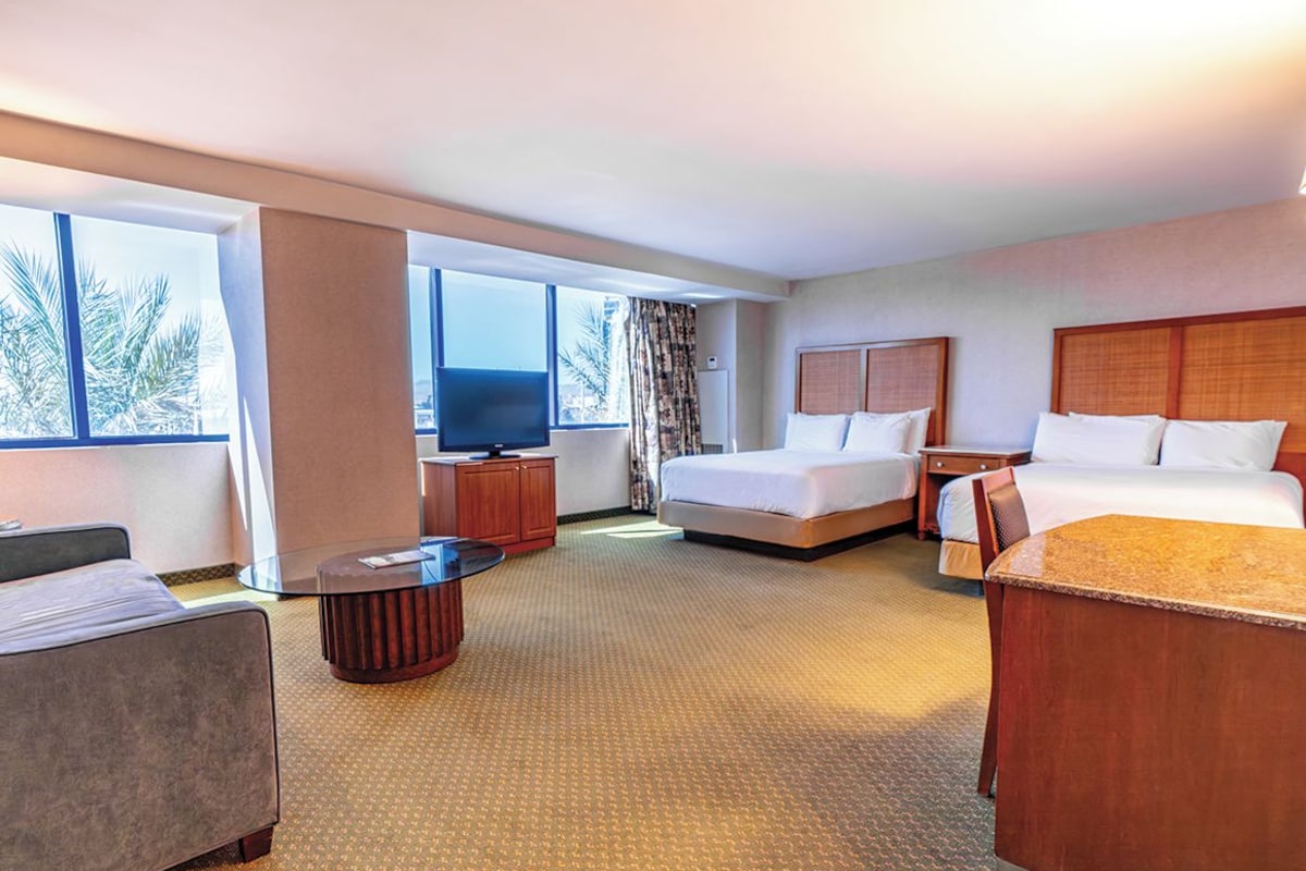 A hotel room with a bed, a desk, a chair, a TV, and large windows.