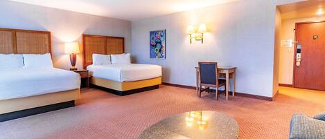 A hotel room with two beds, a round table, a chair, a small desk, and a painting on the wall.