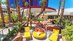 A poolside area with yellow lounge chairs, a round table with a colorful cushion, and a rock formation. - Masquerade Tower at Rio Hotel & Casino (Las Vegas)