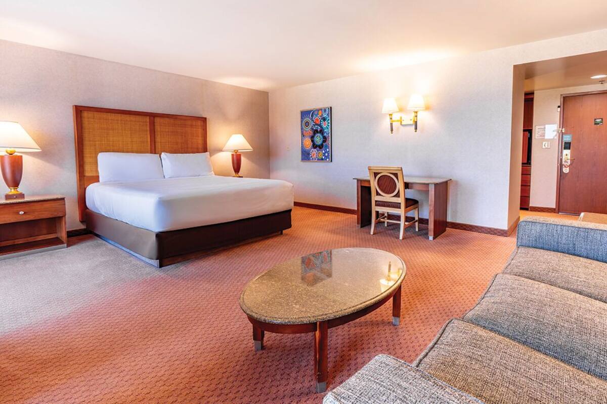 A hotel room with a bed, a desk, a chair, a small table, and a sofa.