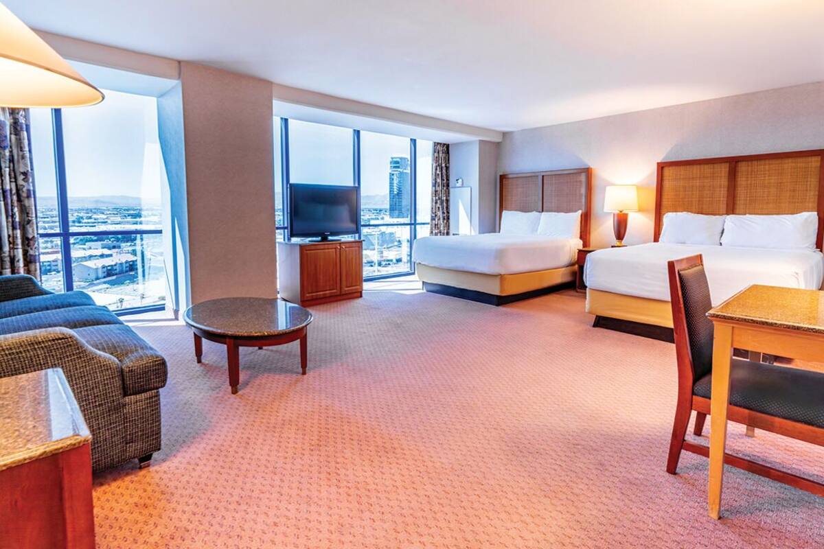 A hotel room with a bed, a sofa, a table, a TV, and large windows with a city view.