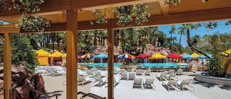 A pool area with lounge chairs and umbrellas, surrounded by palm trees and a rocky backdrop.