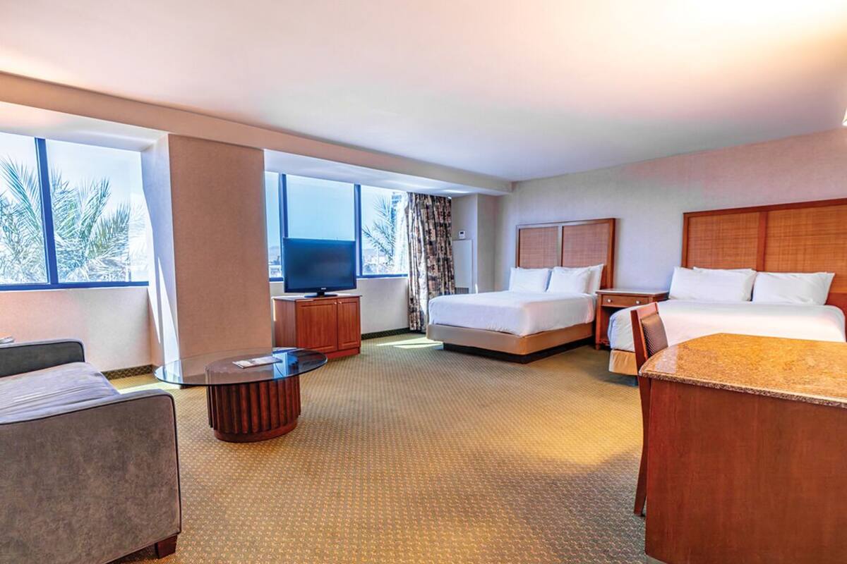 A hotel room with a bed, a desk, a chair, a TV, and large windows.