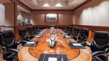 Une salle de conférence avec une longue table, des fauteuils en cuir noir et un arrangement floral au centre.