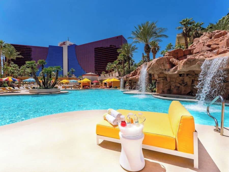 A pool area with a waterfall feature, lounge chairs, and a view of a large building in the background.