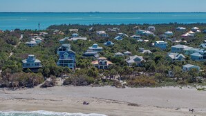 Zona residencial costera con casas rodeadas de vegetación densa y una playa en primer plano.