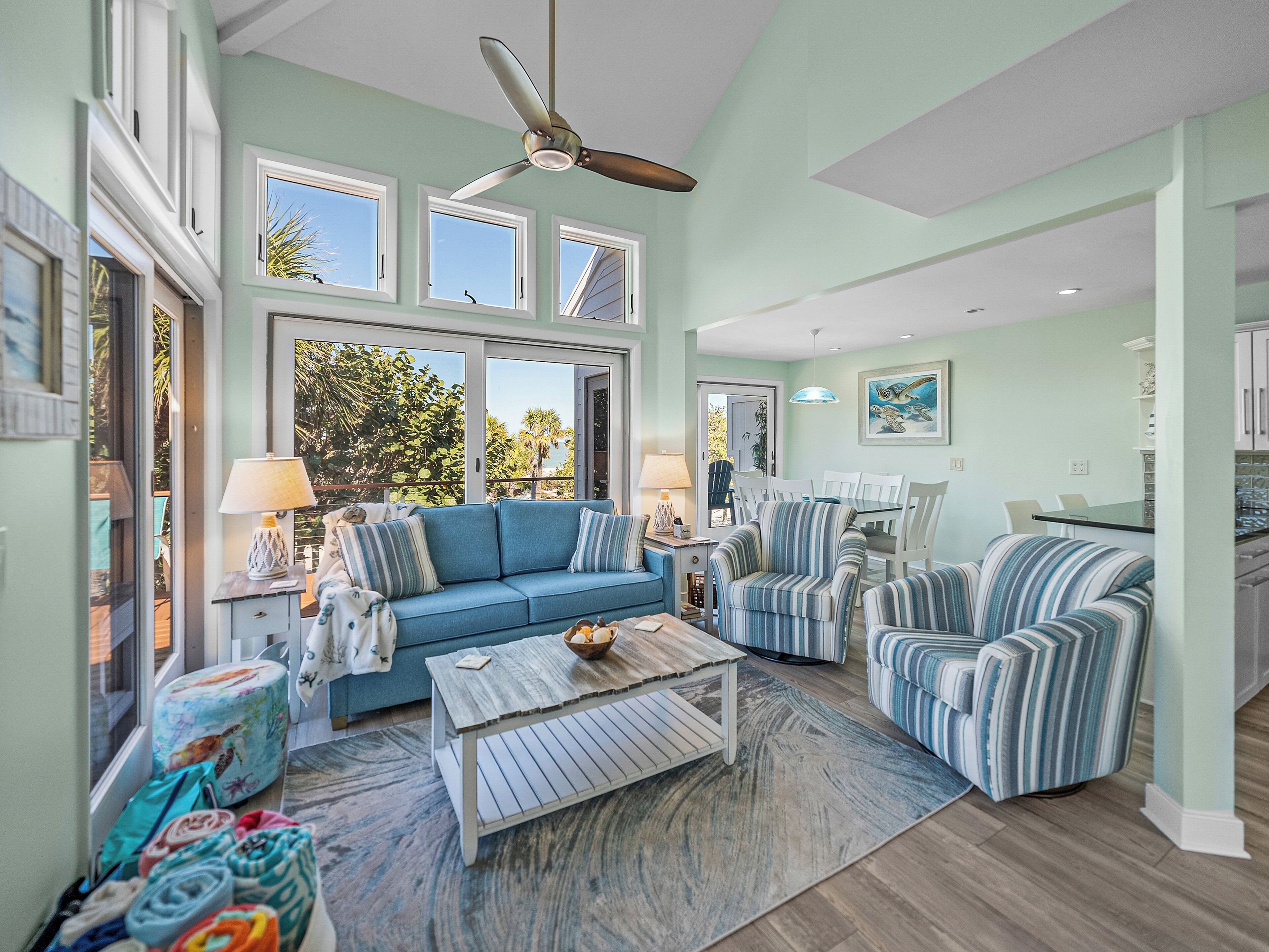 A spacious living room with a blue sofa, striped armchairs, a wooden coffee table, and a ceiling fan.