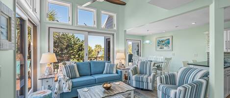 A spacious living room with a blue sofa, striped armchairs, a wooden coffee table, and a ceiling fan.