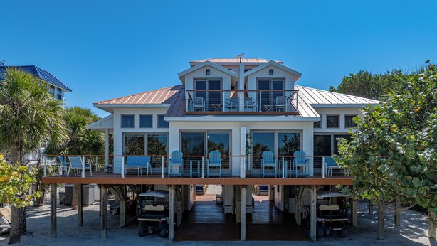 Una casa frente a la playa con balcón, múltiples ventanas y un espacio de terraza cubierto.