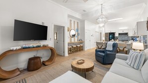 A modern living room with a flat-screen TV, a wooden console, a round coffee table, a blue armchair, and a sofa.