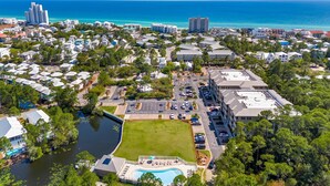 An aerial view of a coastal residential area with a large swimming pool, multiple buildings, and a clear view of the ocean.