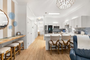 A modern kitchen with white cabinets, a central island, bar stools, and a chandelier.