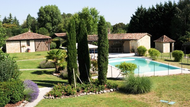 Propiedad residencial con piscina, jardín y varios edificios con techos de tejas.