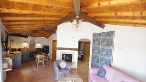 Un amplio salón con techo de madera, chimenea, sofá rosa y zona de comedor con mesa y sillas.