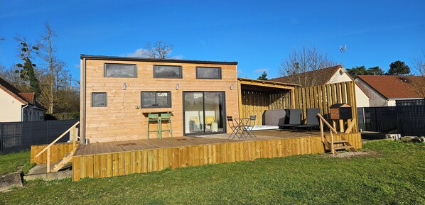 Una casa de madera de dos pisos con un balcón, mobiliario exterior y un ventanal grande.