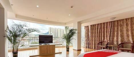 A hotel room with two beds, a TV on a wooden cabinet, and a balcony with a view of tall buildings.