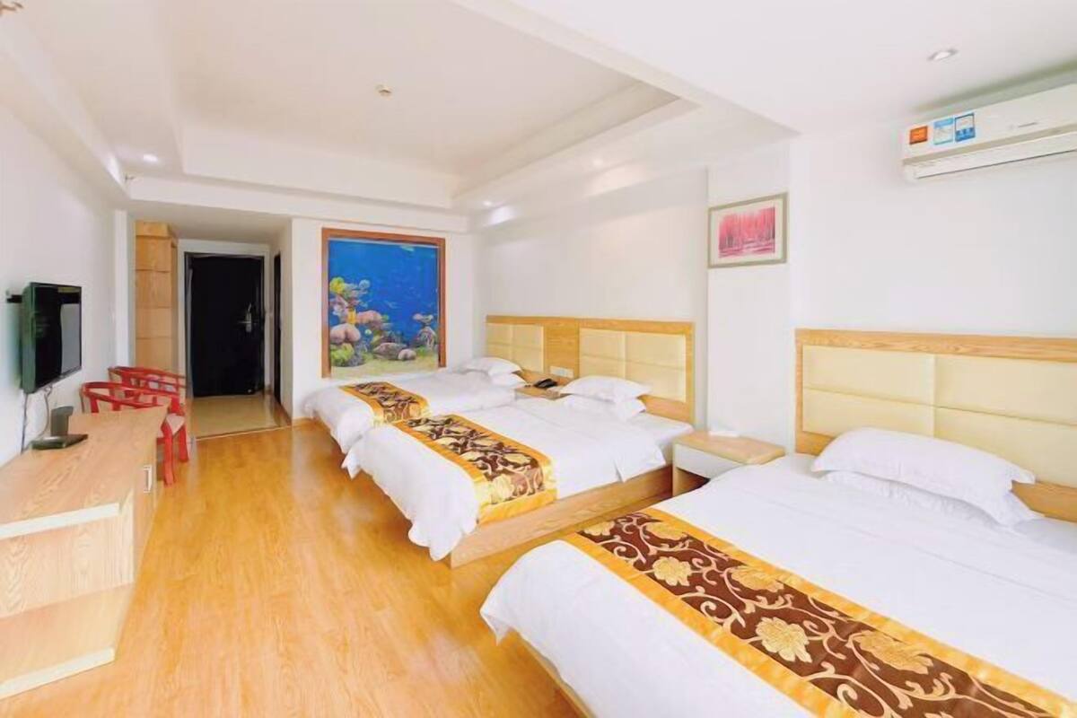 Een hotelkamer met twee bedden, een houten bureau, een televisie en een schilderij van vissen aan de muur.