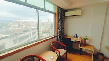A room with a large window, a desk, a chair, and a small table.