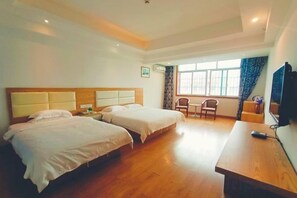 Habitación de hotel con dos camas, un escritorio de madera, una silla, un televisor y una ventana con cortinas.