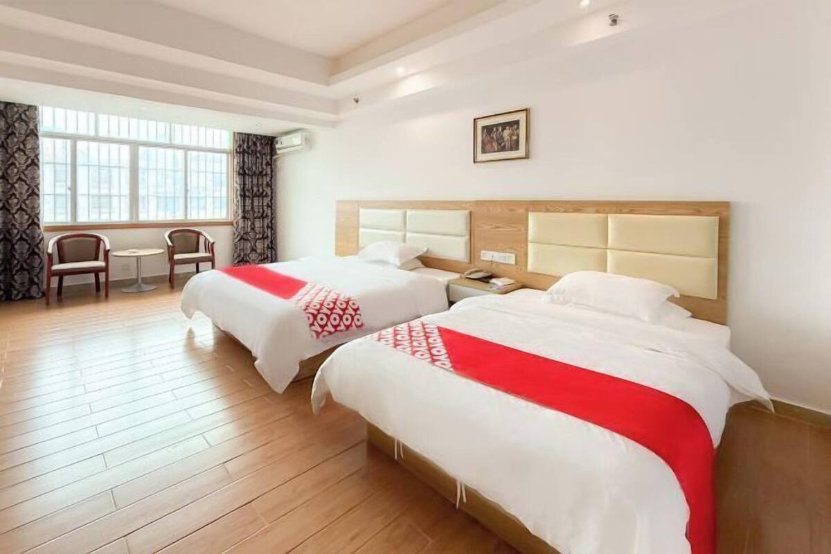 Een hotelkamer met twee bedden, een tafeltje, stoelen en een raam met gordijnen.