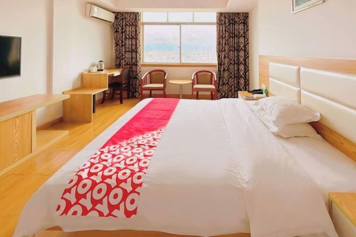 Een hotelkamer met een bed, een bureau, twee stoelen, een kleine tafel, een televisie en een raam met gordijnen.