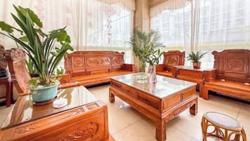 A traditional wooden furniture set with a glass-top coffee table, a sofa, and a chair, accompanied by potted plants.