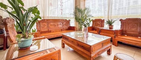Conjunto de móveis de madeira tradicional com mesa de centro de vidro, sofá e poltrona, acompanhados por plantas em vasos.