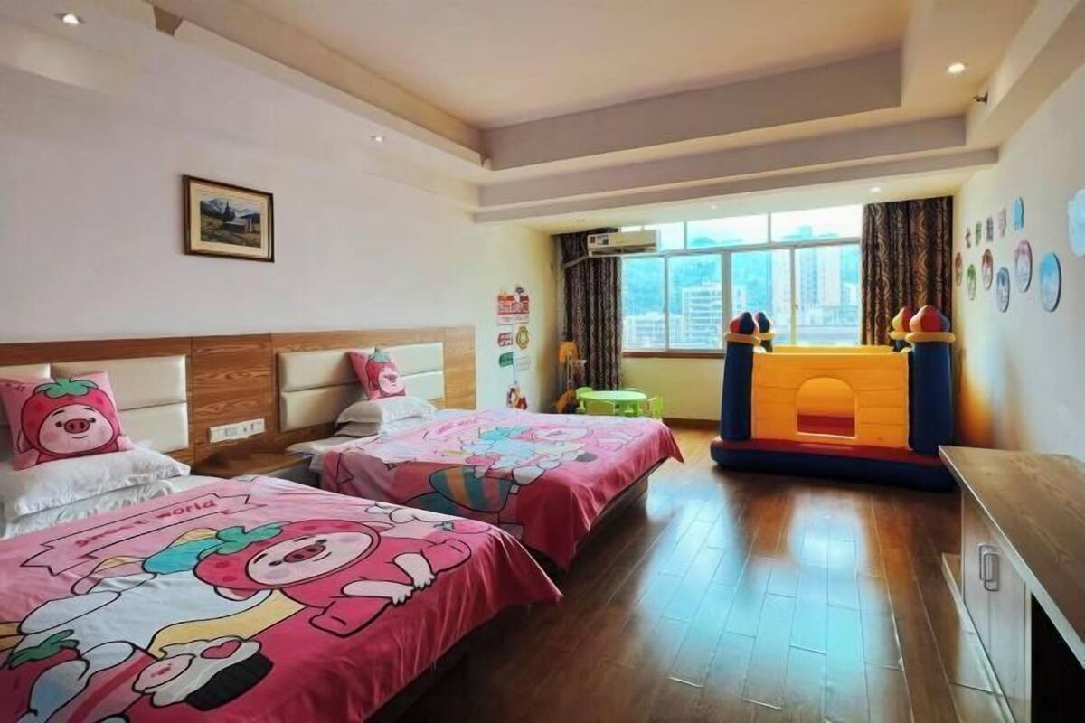 Een hotelkamer met twee bedden, een reisbedje, een raam met gordijnen en een muur met diverse decoraties.