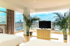 Quarto de hotel com uma janela grande, cama, televisão e plantas em vasos.