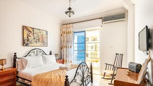A bedroom with a bed, a desk, a chair, a television, and a painting on the wall.