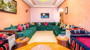 A living room with a green sofa set, a flat-screen TV mounted on the wall, and a decorative ceiling light.
