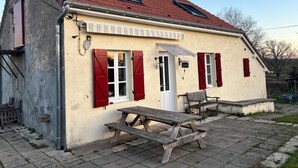 Een landelijk gebouw met een rode pannendak, een houten bank en een picknicktafel.