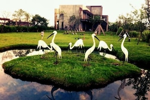A pond with white statues of birds, a grassy area, and a building in the background. - Serene Gray Bed & Breakfast (Yilan)