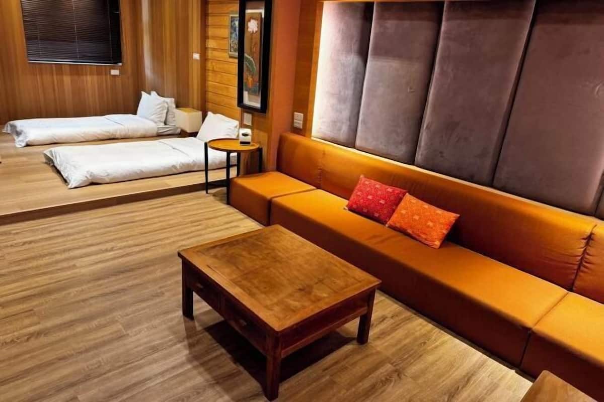 A room with a wooden floor, a sofa with a cushion, a small table, and a bed with pillows.