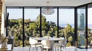 A modern dining area with a round table and chairs, large windows offering a view of trees and buildings, and a pendant light.