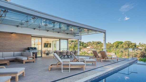 A modern outdoor pool area with lounge chairs, a dining area, and a view of the surrounding landscape.
