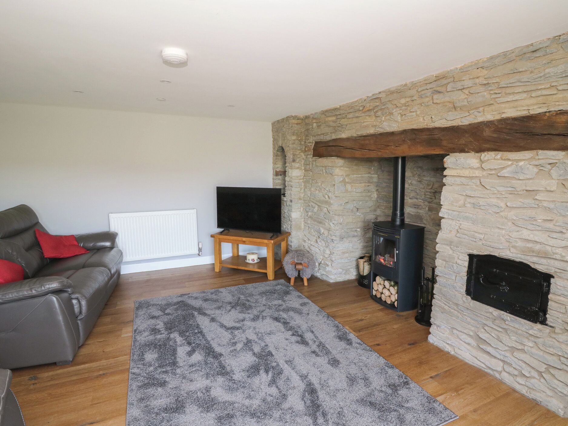 Una sala de estar con chimenea de piedra, un sofá de cuero, un televisor sobre un mueble de madera y una alfombra gris.