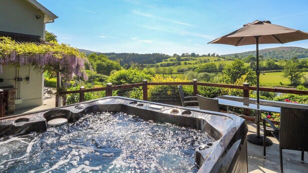 Een hottub met uitzicht op een groen landschap, een houten hek en een parasol.