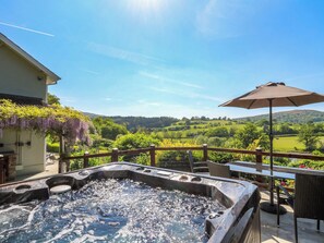 Ein Whirlpool mit Blick auf eine grüne Landschaft, einen Holzzaun und einen Sonnenschirm.