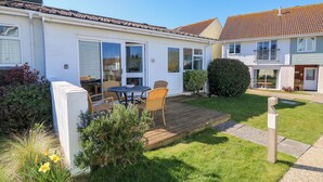 Ein zweigeschossiges Haus mit einer Terrasse, einem Essbereich mit Stühlen und einem kleinen Garten mit Blumen.