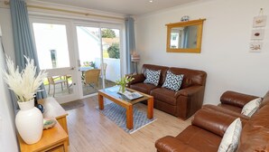 Ein Wohnzimmer mit braunem Ledersofa, einem Holztisch und einer Glasdoor zu einer Außenveranda.