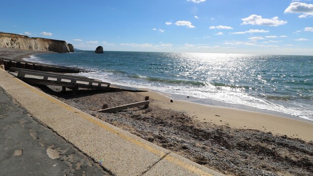 Ein Strand mit einer Holzpromenade, einer felsigen Küstenlinie und einer Klippe im Hintergrund.