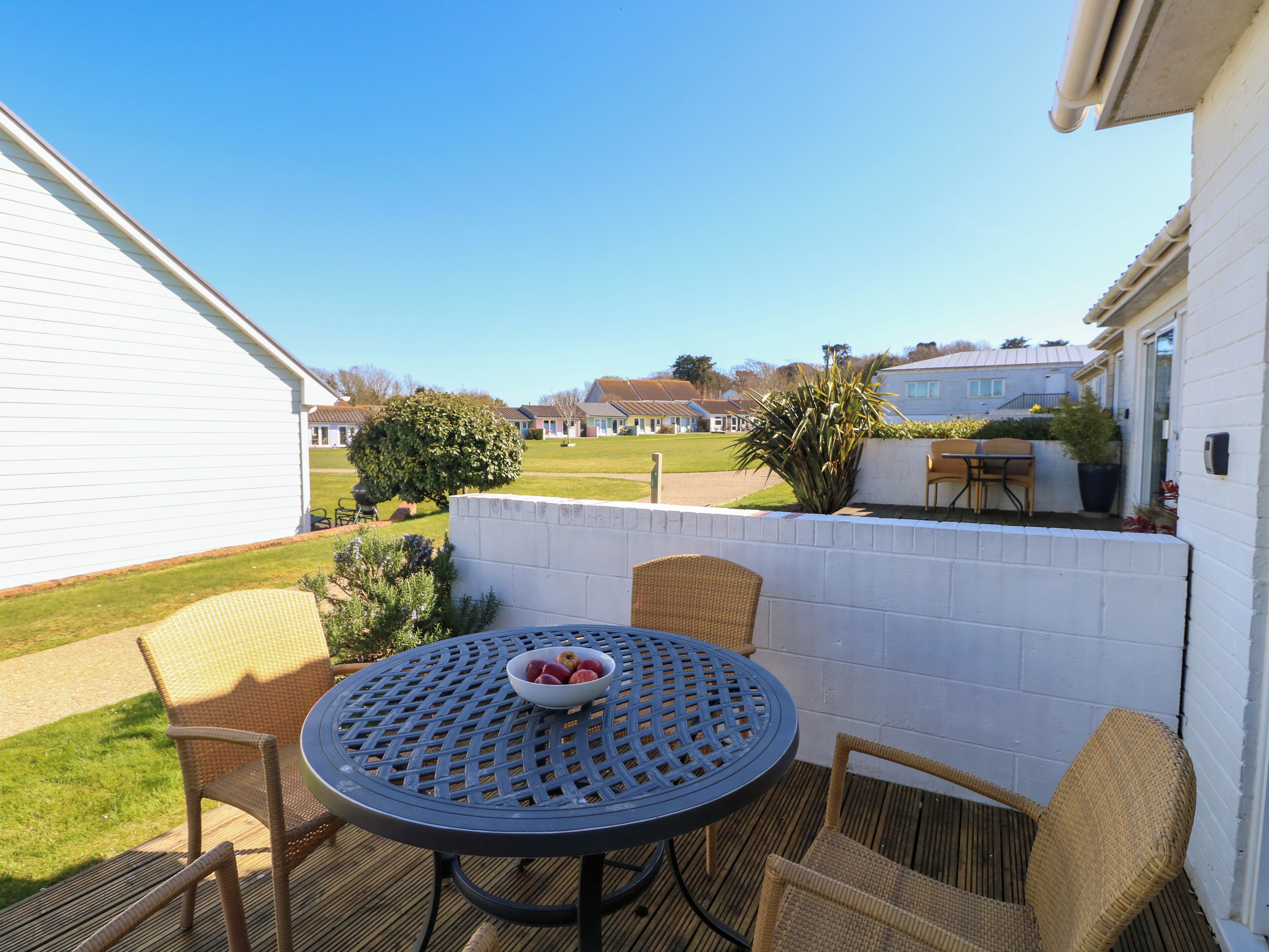 Une terrasse avec des chaises et une table en osier, un saladier rempli de fruits et, au loin, une vue sur des maisons.