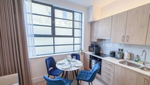 Eine moderne Küche mit Essbereich, ausgestattet mit einem runden Tisch und Stühlen, einem Einbauofen und einem Fenster mit Jalousien.