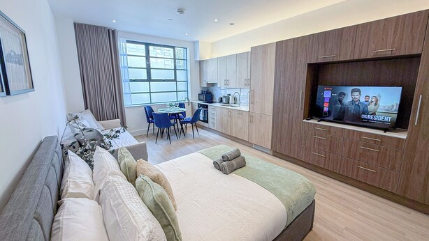 Ein modernes Hotelzimmer mit einem großen Bett, einem Essbereich und einem Fernseher, der 'The Resident' zeigt.