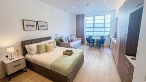 Ein modernes Hotelzimmer mit einem großen Bett, einer Sitzecke mit einer Couch, einem Esstisch und einer Küchenzeile.