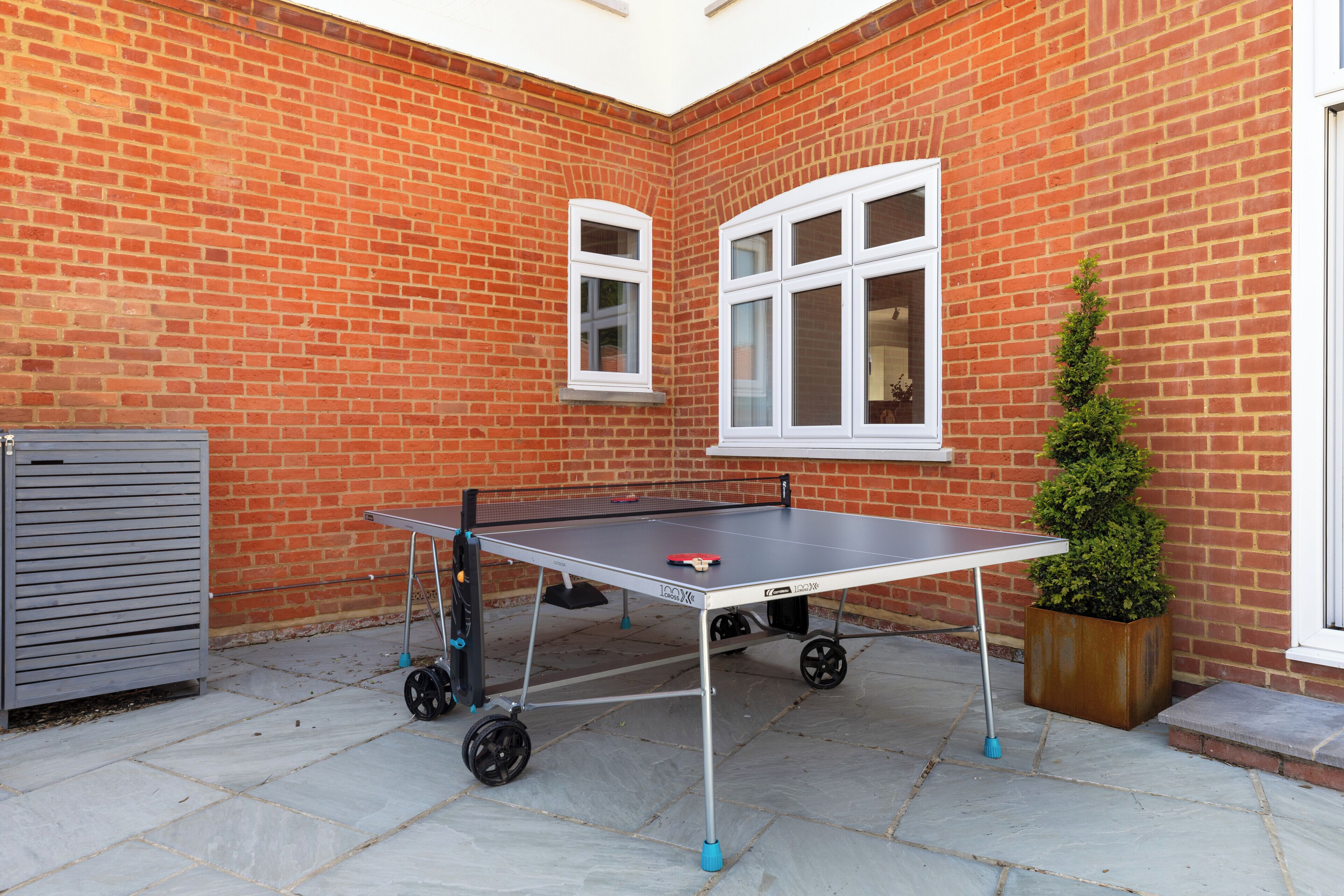 Una mesa de ping pong en un patio con un muro de ladrillo y una ventana.