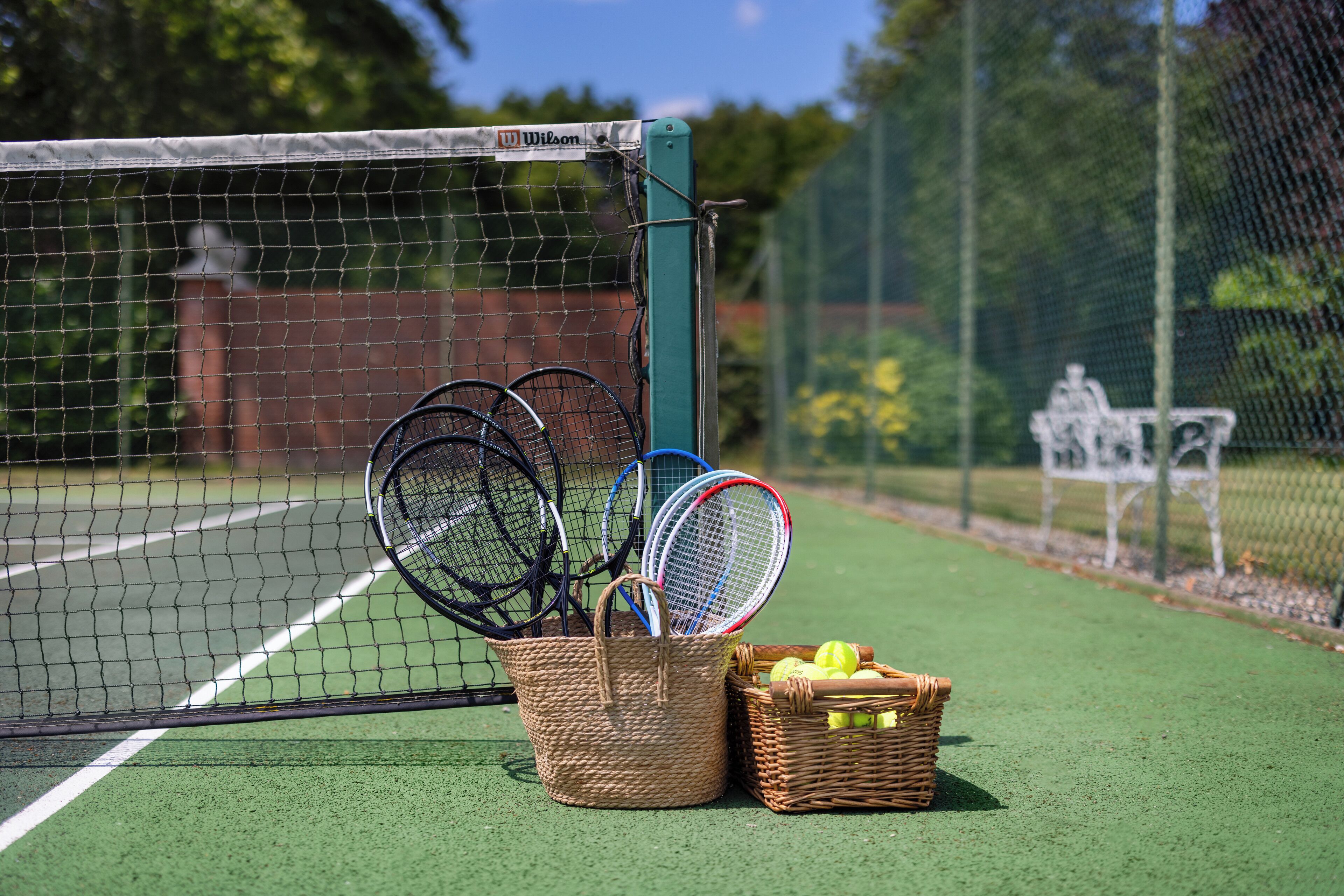 A tennis court with a basket of tennis rackets and a basket of tennis balls.